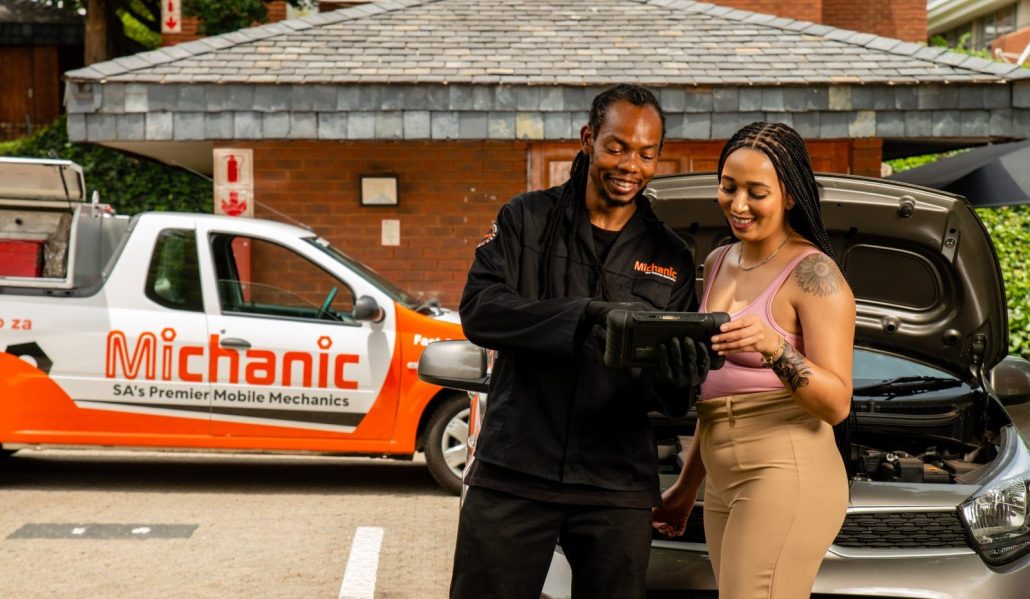 A Michanic mobile mechanic going through the digital service record with a Honda owner on site, with the Michanic service vehicle alongside
